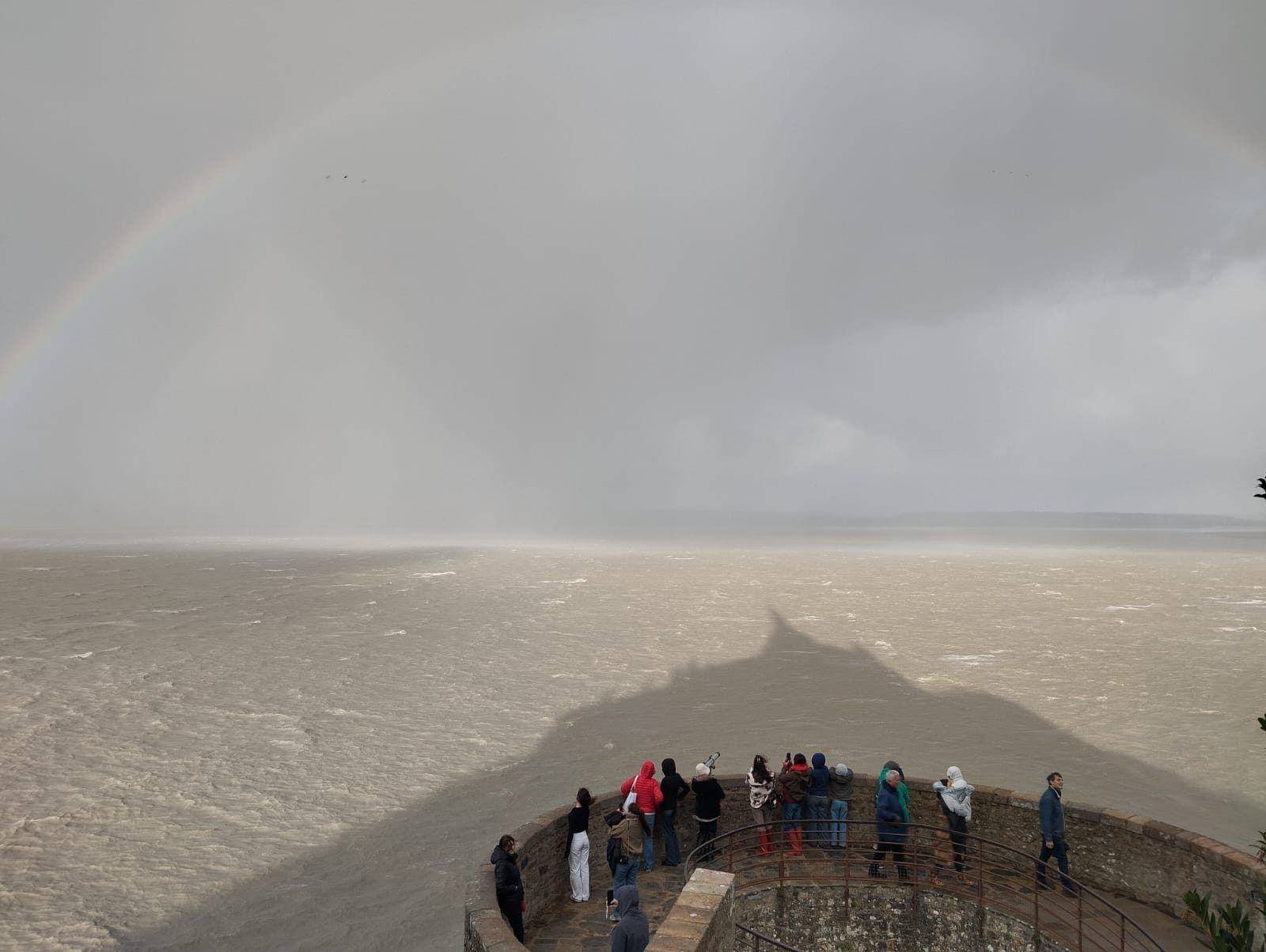 La baie sous la tempête : l'ombre du Mont se projette sur l'eau, sous un arc-en-ciel.